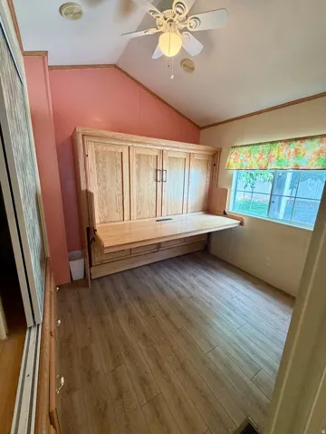 Unfurnished office featuring vaulted ceiling, a ceiling fan, light wood-style flooring, and ornamental molding