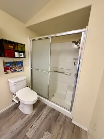 Full bath featuring a stall shower, vaulted ceiling, and light wood-style floors