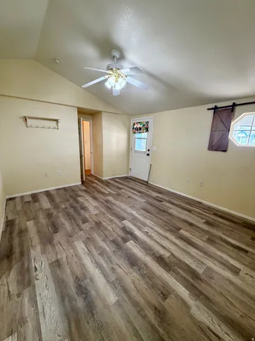 Unfurnished living room featuring a barn door, dark wood finished floors, ceiling fan, and healthy amount of natural light