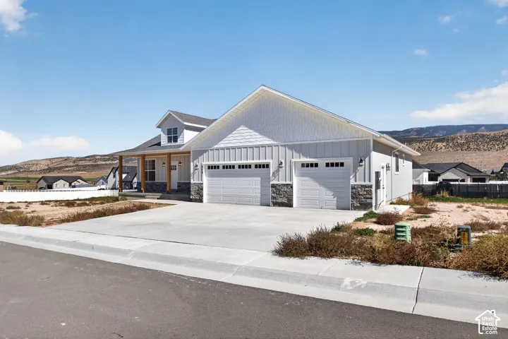 Single-family residence featuring a two-car garage with carriage-style doors, board and batten siding, stone accents, a covered front porch with exposed wood columns, and a concrete driveway
