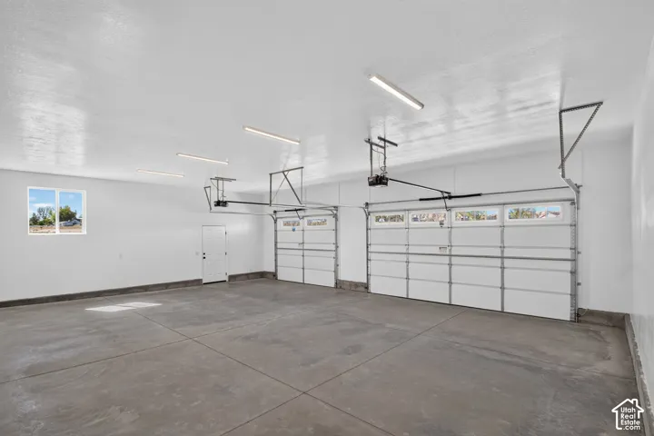 Spacious three-car garage featuring automatic openers, overhead fluorescent lighting, a side access door, and a high-set window