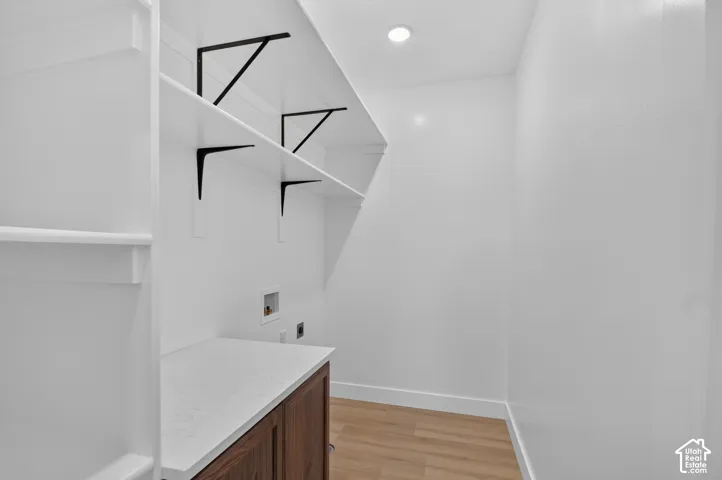 Utility space featuring wood-finish flooring, white walls, built-in shelving with black brackets, a built-in countertop, and an integrated cabinet