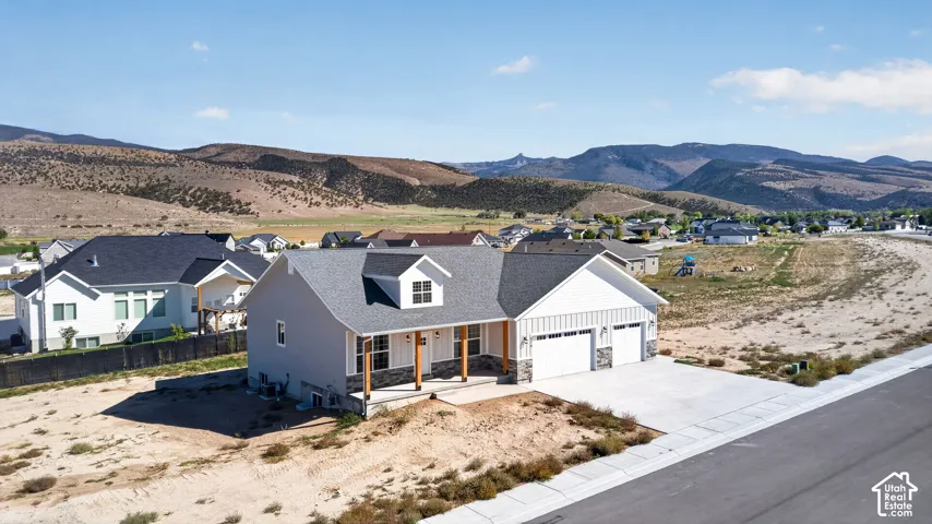 Single-story residence featuring light gray siding with white board and batten accents, a dark gray shingled roof, a two-car garage, and stone veneer detailing on the exterior