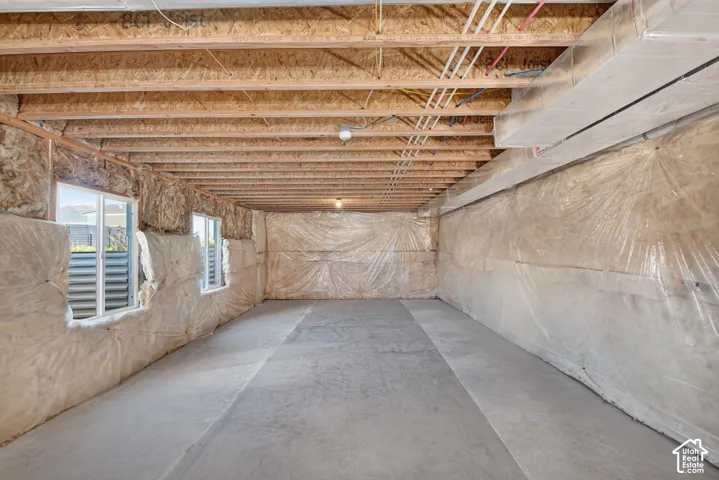 Unfinished basement with exposed ceiling joists, concrete flooring, and multiple windows