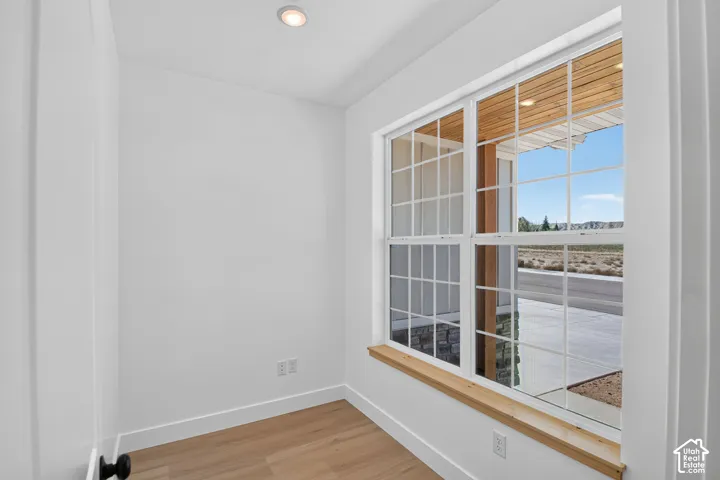 Recessed ceiling lighting, wood-finish flooring, white trim, white door with matte black hardware, and a window with a wood sill