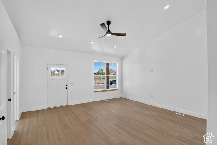 Vaulted ceiling with recessed lighting, wood-finish flooring, white paneled entry door with glass inserts, and a modern ceiling fan