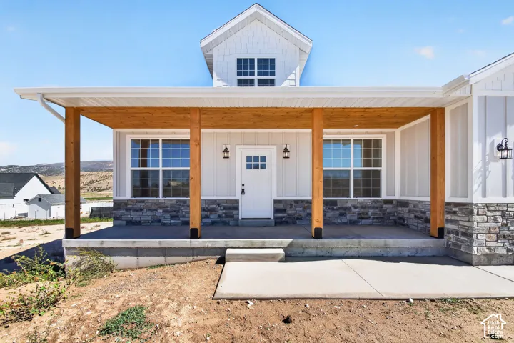 Covered porch with wood beams and ceiling, stone veneer accents, white board-and-batten siding, and a white entry door