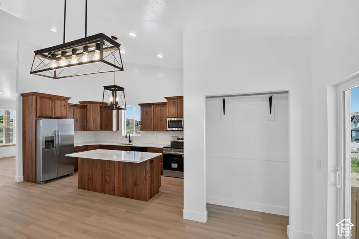 Kitchen featuring wood cabinetry, stainless steel appliances, a center island with a light-colored countertop, and two black-framed linear chandeliers