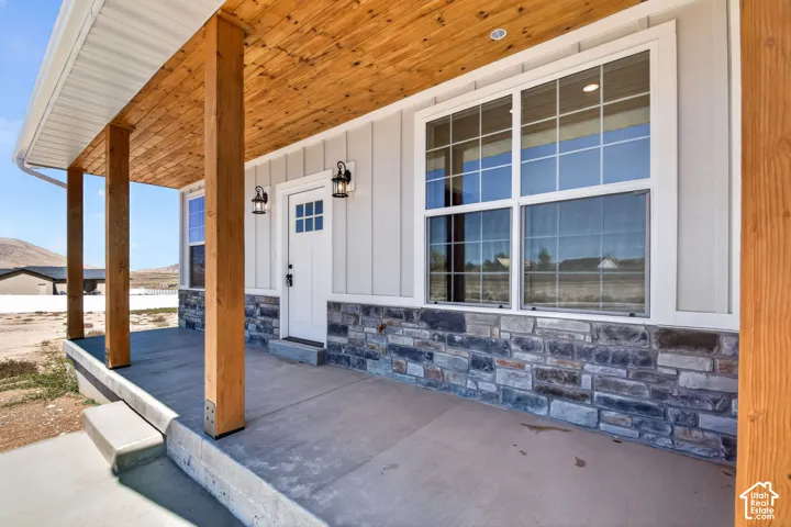 Covered front porch with wood-finish ceiling, stone veneer accents, and white vertical siding