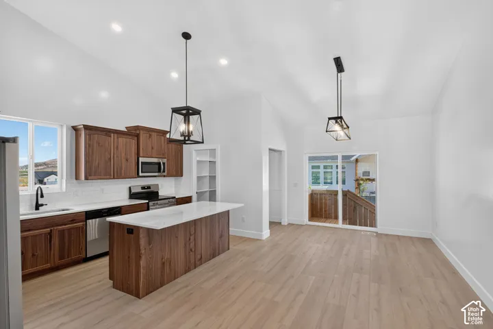 Vaulted ceilings, wood-finish flooring, kitchen island with solid surface countertop, stainless steel appliances, and sliding glass door