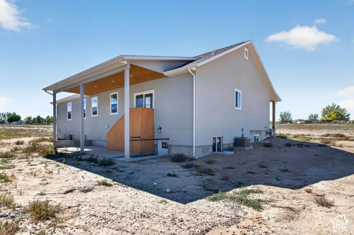 Exterior featuring a covered patio with a wood-finish ceiling, stucco siding, multiple windows, and a basement entry