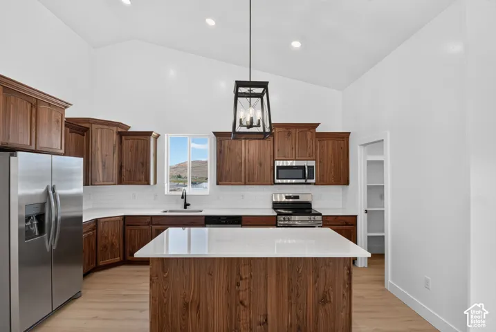 Vaulted ceiling kitchen featuring wood-finish cabinetry, white countertops, stainless steel appliances, and wood-finish flooring