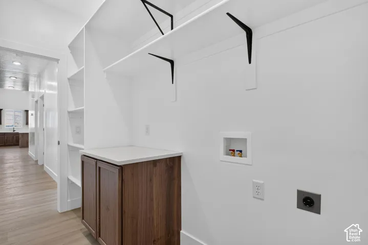 Integrated laundry area featuring white shelving, a wood-finish cabinet with a light-toned countertop, and light wood-finish flooring