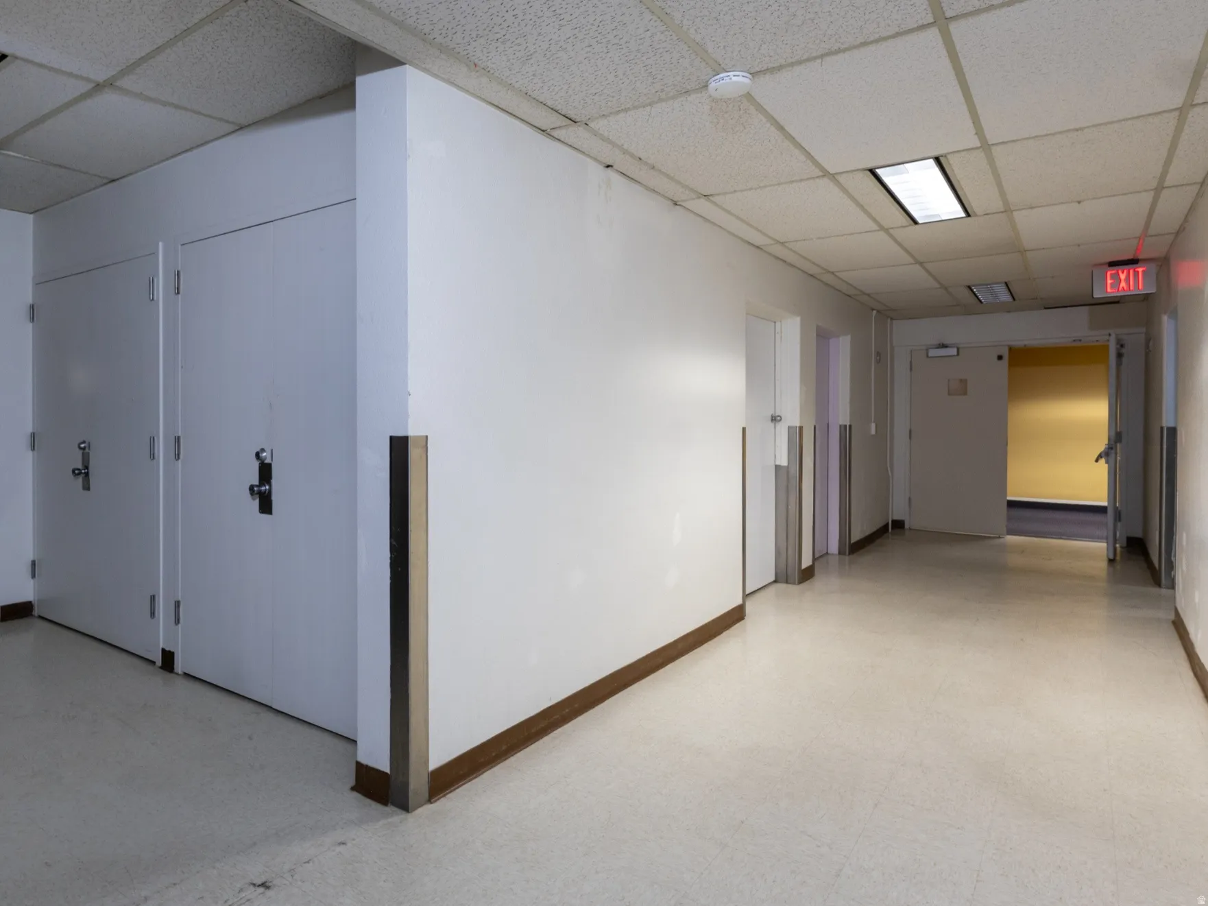 Commercial hallway with light-colored flooring, white walls, and a suspended acoustic tile ceiling