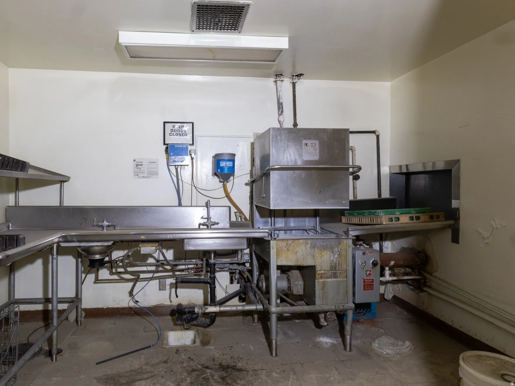 Commercial-grade stainless steel dishwashing station featuring multiple sinks, an industrial dishwasher, and extensive stainless steel shelving