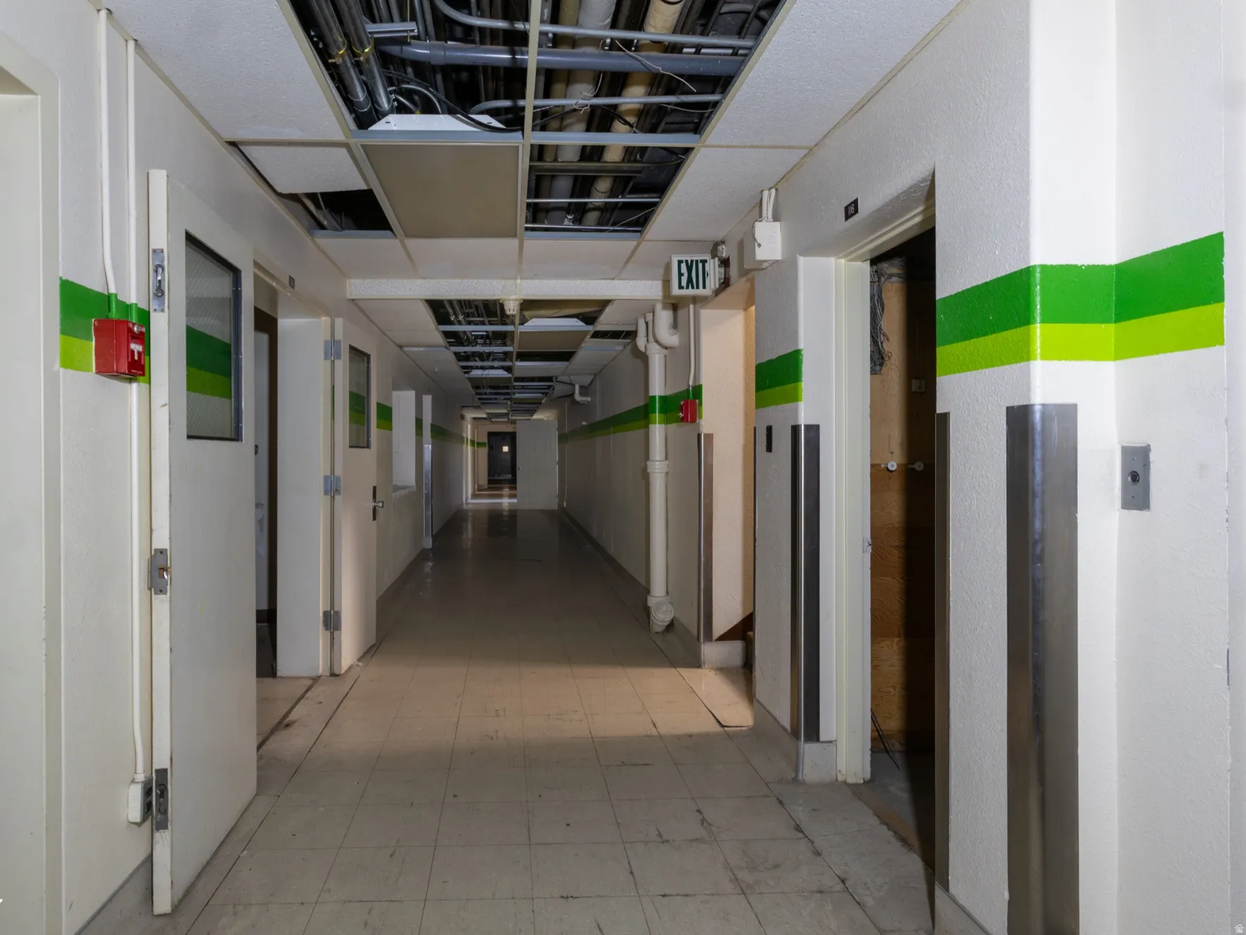 Long corridor with white walls, green striped accents, and a tiled floor