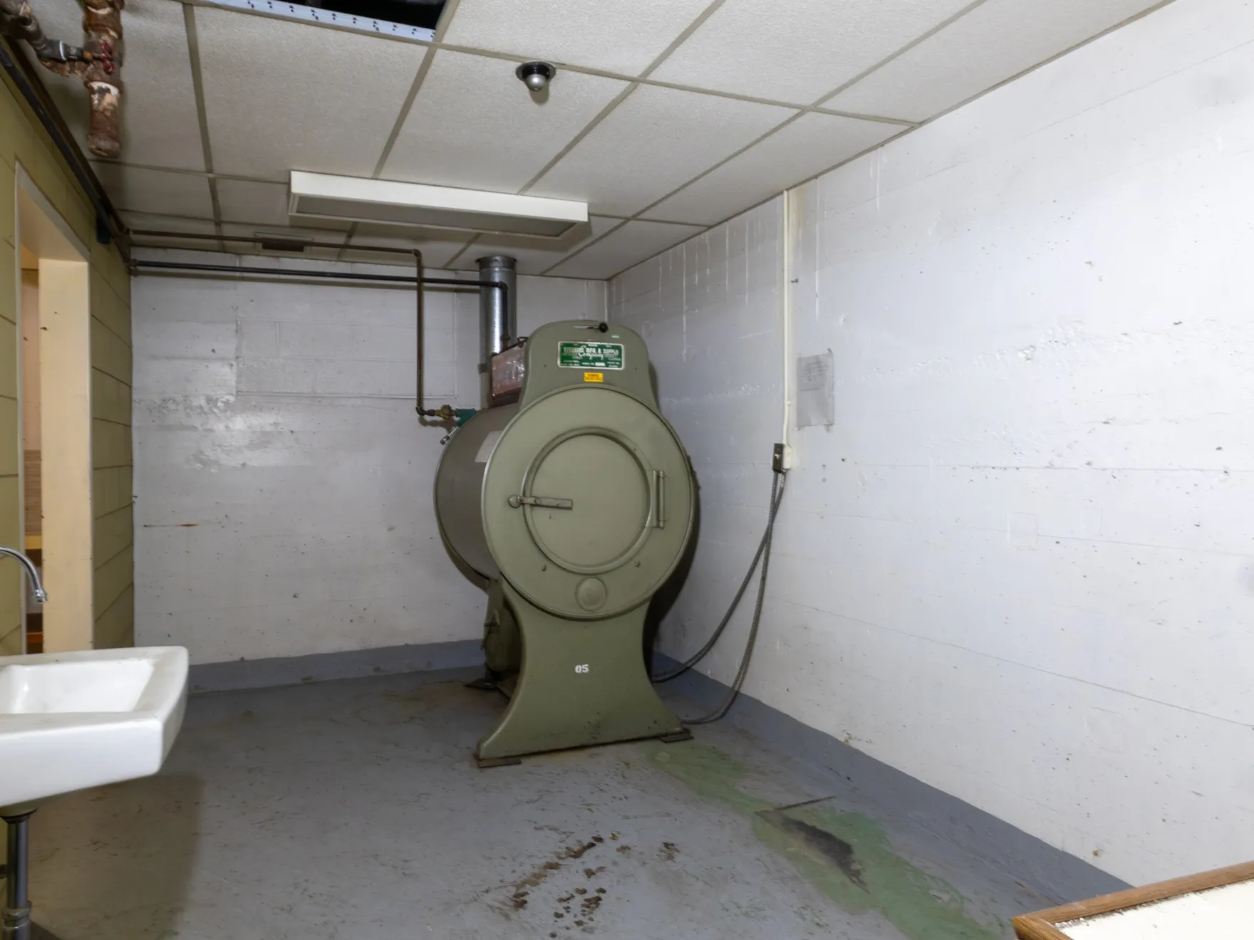 Utility space featuring a wall-mounted sink with chrome fixtures, an industrial-style machine, painted concrete block walls, and a suspended acoustic tile ceiling