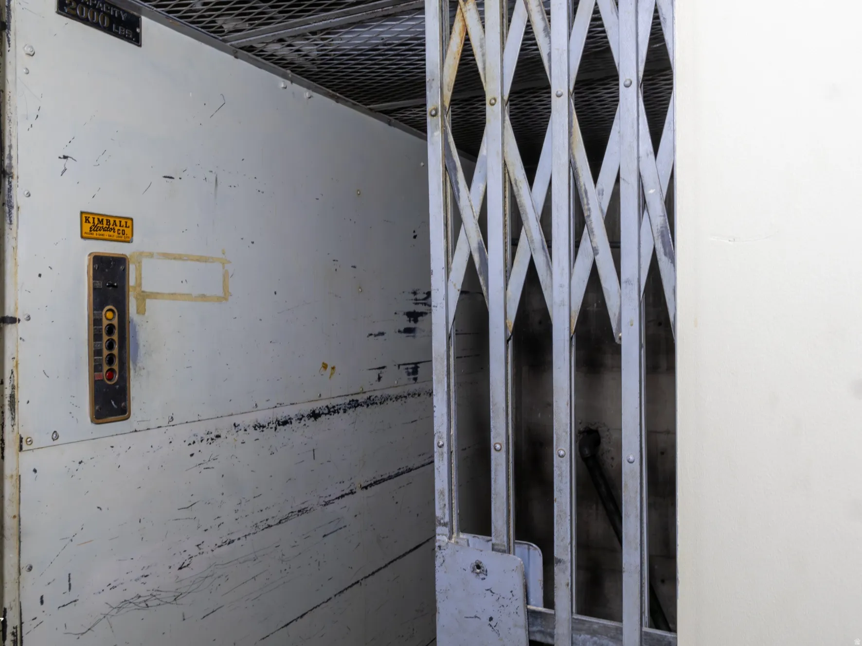 Industrial freight elevator with a capacity of 2000 lbs, featuring a diamond-patterned gate and a control panel with multiple buttons