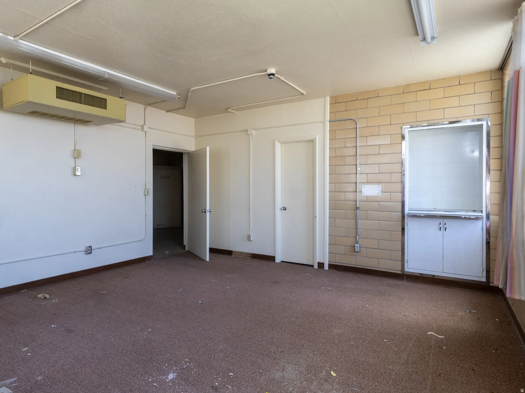 Interior space featuring a dropped ceiling with fluorescent lighting, industrial-style wall-mounted air conditioning unit, and a built-in cabinetry unit with a white countertop and base cabinets