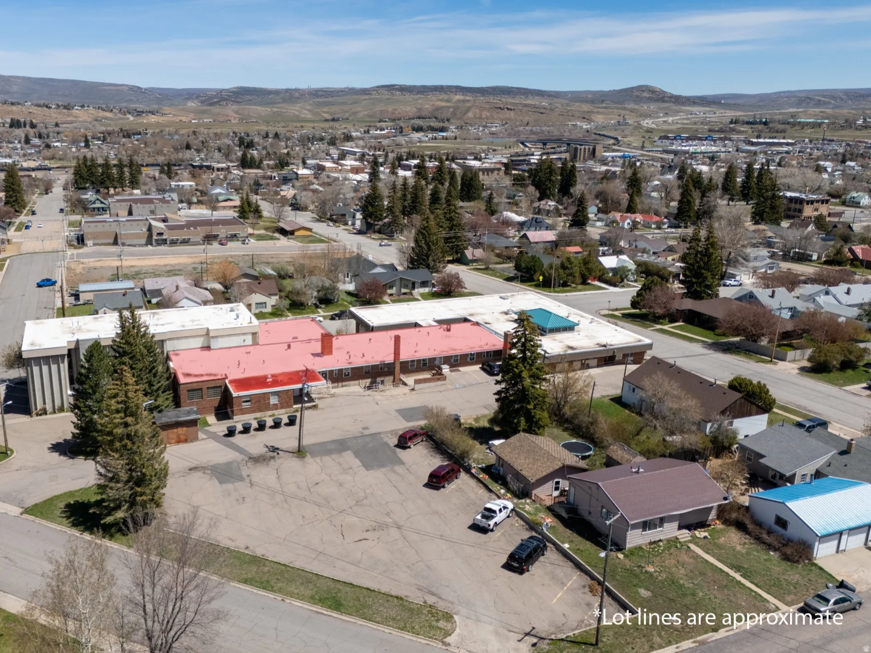 Aerial perspective showcasing a commercial building with a red roof, a large parking area, and surrounding mixed-use properties