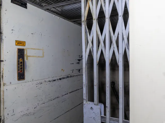 Industrial freight elevator with a capacity of 2000 lbs, featuring a diamond-patterned gate and a control panel with multiple buttons