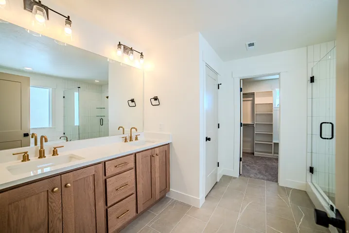 Bathroom with double vanity, a walk in closet, a shower stall, and light tile patterned floors