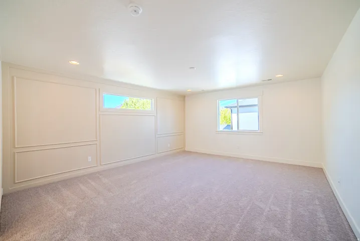 Empty room with light colored carpet, healthy amount of natural light, a decorative wall, a smoke detector, and recessed lighting