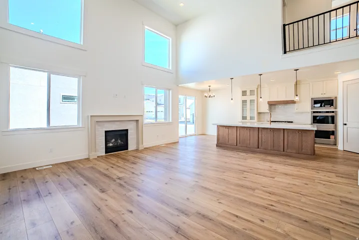 Unfurnished living room featuring a fireplace, hanging lights, light wood-type flooring, and a high ceiling