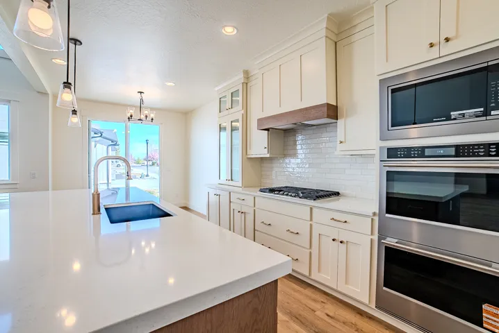 Kitchen featuring stainless steel appliances, suspended lighting, light stone countertops, light wood-type flooring, and glass insert cabinets