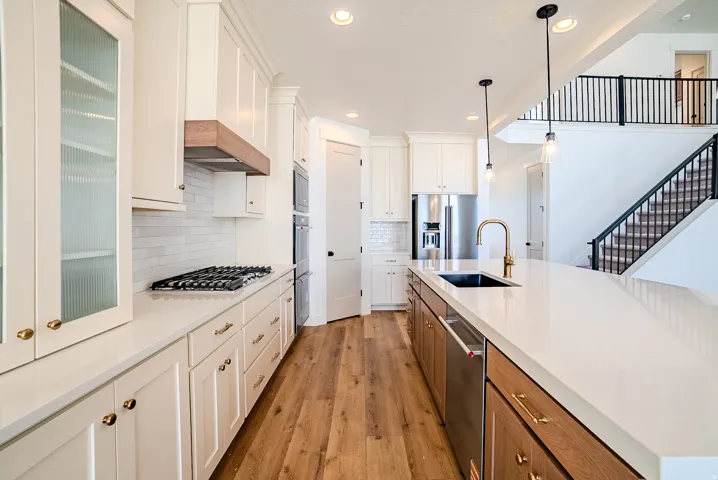Two tone kitchen featuring light wood-style flooring, stainless steel appliances, two tone cabinets, hanging light fixtures, and backsplash