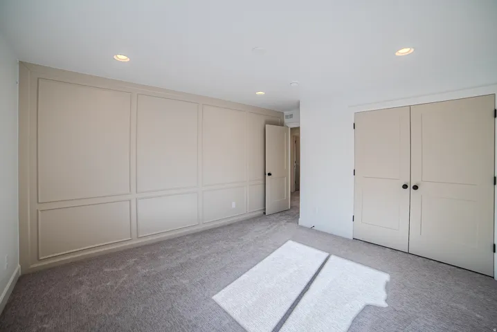 Unfurnished bedroom with a decorative wall, light colored carpet, recessed lighting, and two closets
