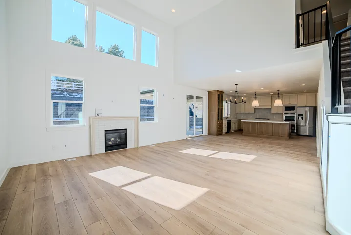 Unfurnished living room featuring a chandelier, a brick fireplace, light wood-type flooring, and a high ceiling