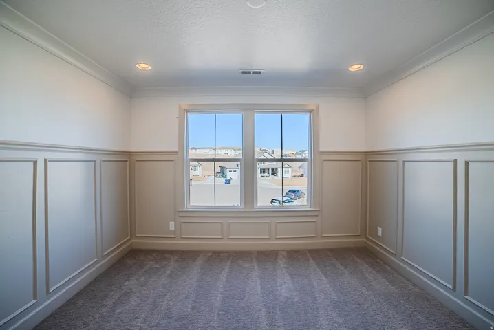 Unfurnished room with a decorative wall, wainscoting, dark colored carpet, and a textured ceiling