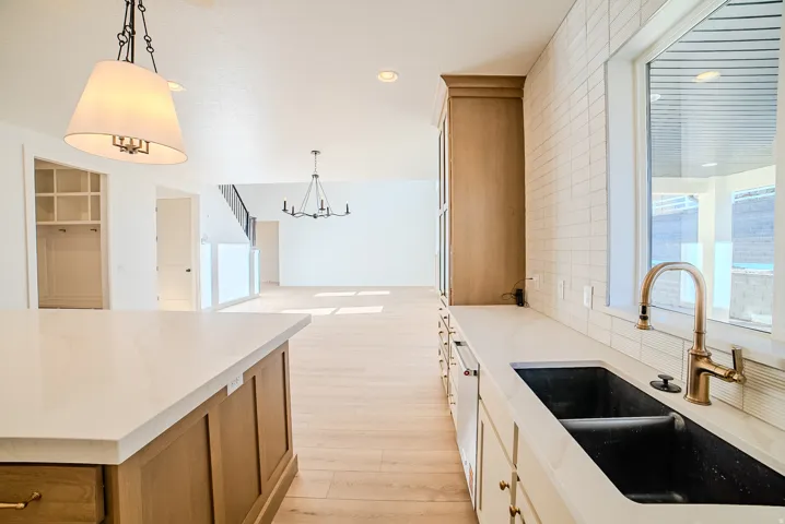 Two tone kitchen featuring light wood-type flooring, light stone counters, a chandelier, two tone color scheme, and backsplash
