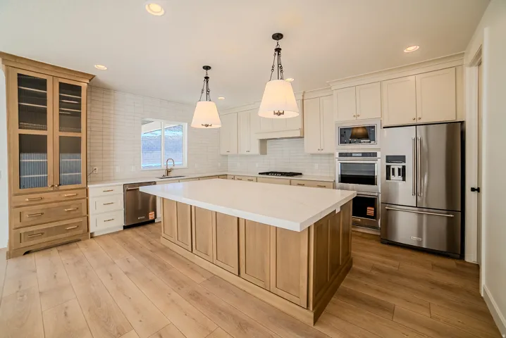 Kitchen featuring dual tone cabinets, stainless steel appliances, a kitchen island, decorative backsplash, and decorative light fixtures