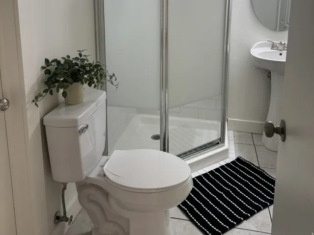 Bathroom featuring a corner glass-enclosed shower with subway tile surround, pedestal sink, and circular mirror