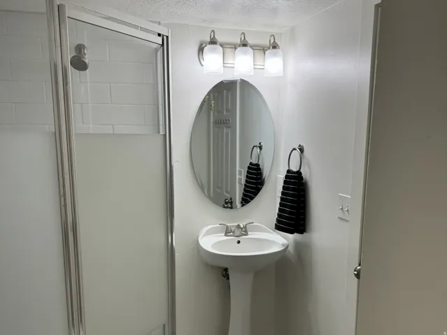Shower bath with a pedestal sink, brushed nickel lighting fixture, and a tiled shower with a glass enclosure