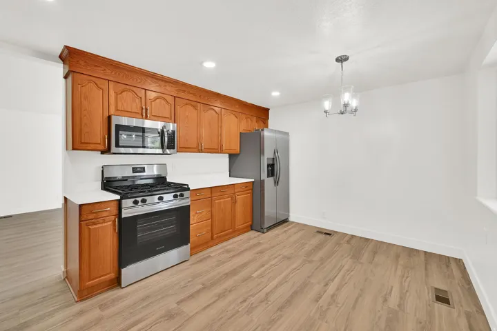 Kitchen with stainless steel appliances, wood finish cabinets, light countertops, light wood-style flooring, and a chandelier