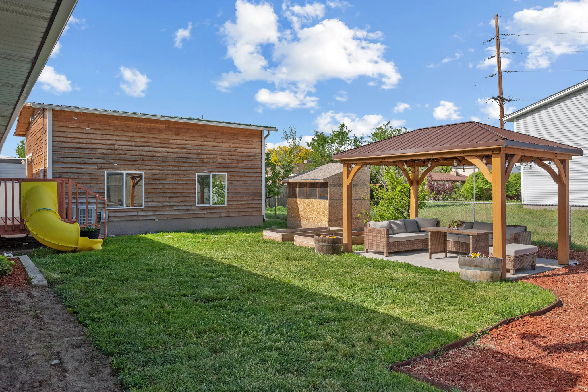 Expansive backyard featuring a large lawn, a wooden gazebo with a metal roof over a concrete patio, and a wooden accessory structure