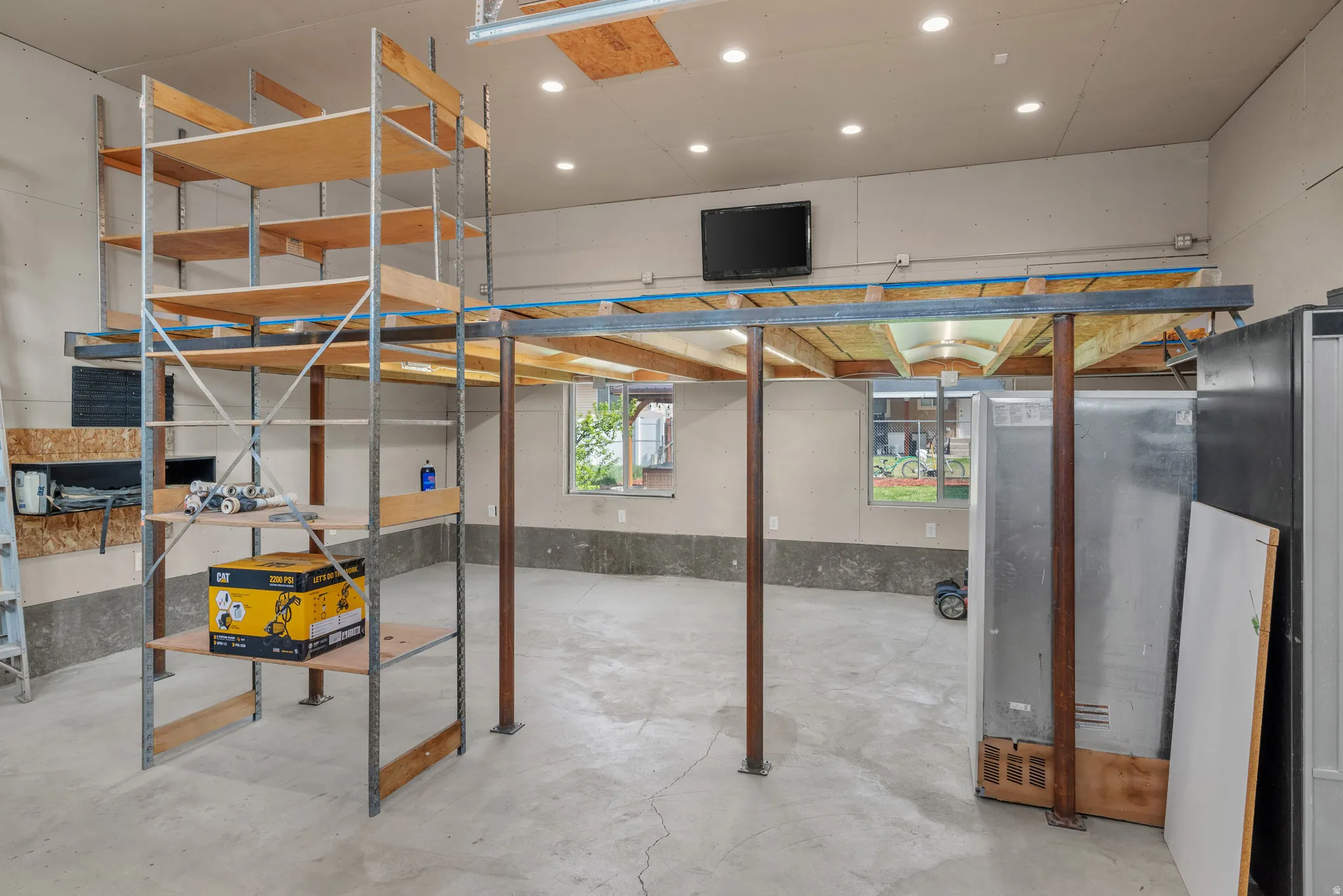 Spacious garage interior featuring high ceilings, concrete flooring, recessed lighting, and multiple windows providing natural light