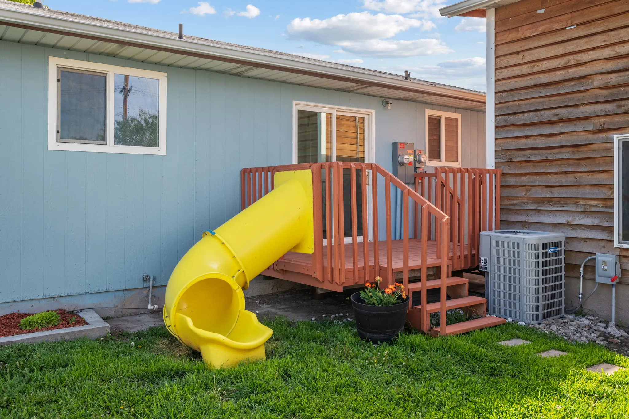 Backyard featuring a wooden deck with railing and stairs, light blue siding, and an exterior heating and air conditioning unit