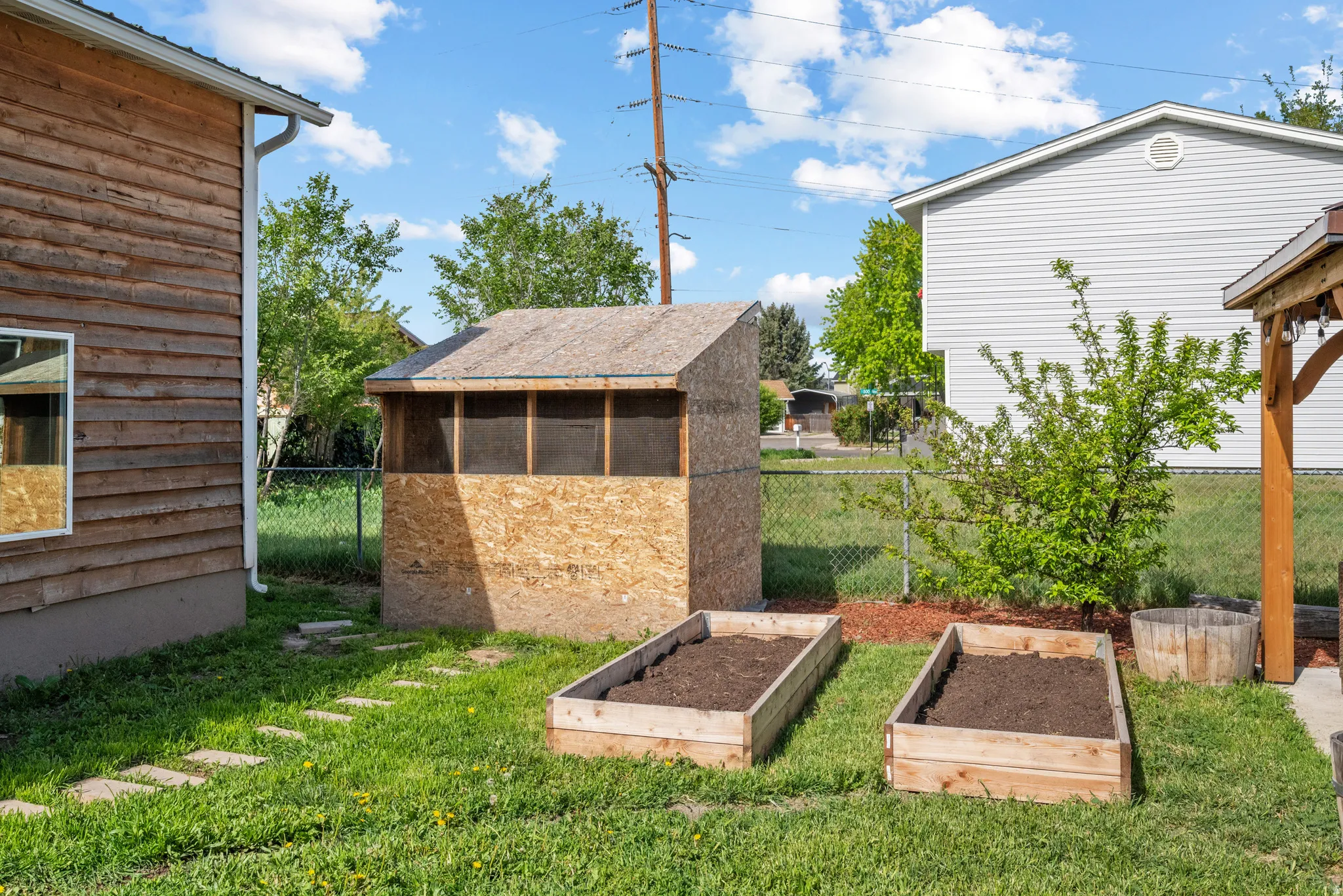 Backyard space featuring a wooden shed with screened openings, two raised garden beds, a mature shrub, and stepping stones
