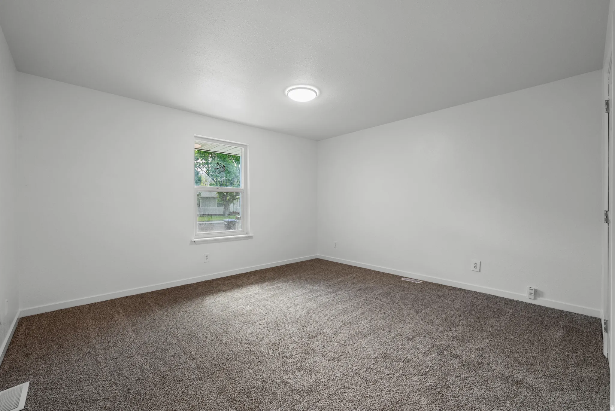 Neutral white wall paint with a single window, overhead flush-mount lighting, and wall-to-wall carpeting
