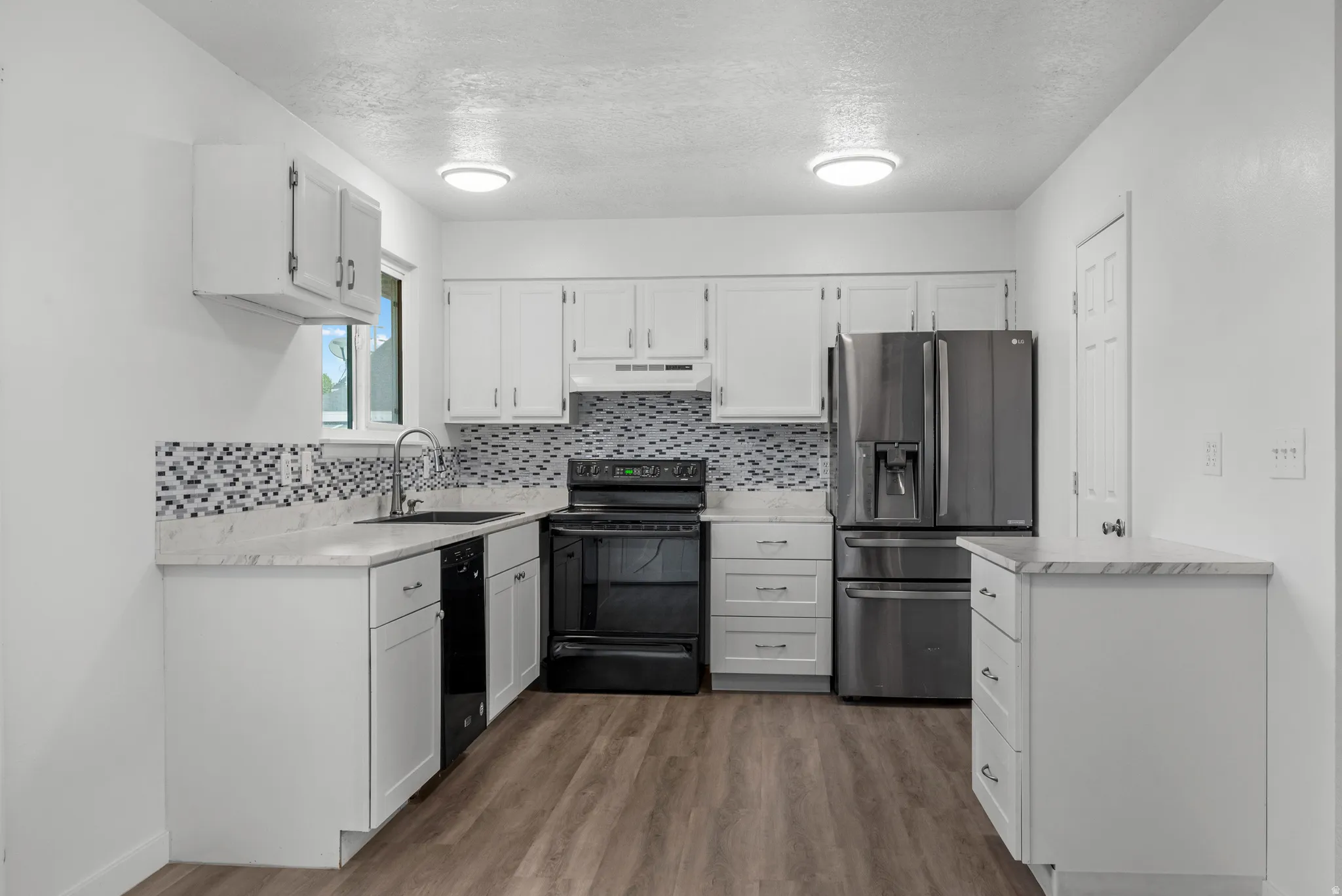 Kitchen featuring white cabinetry, wood-finish flooring, stainless steel refrigerator, black range, and mosaic tile backsplash