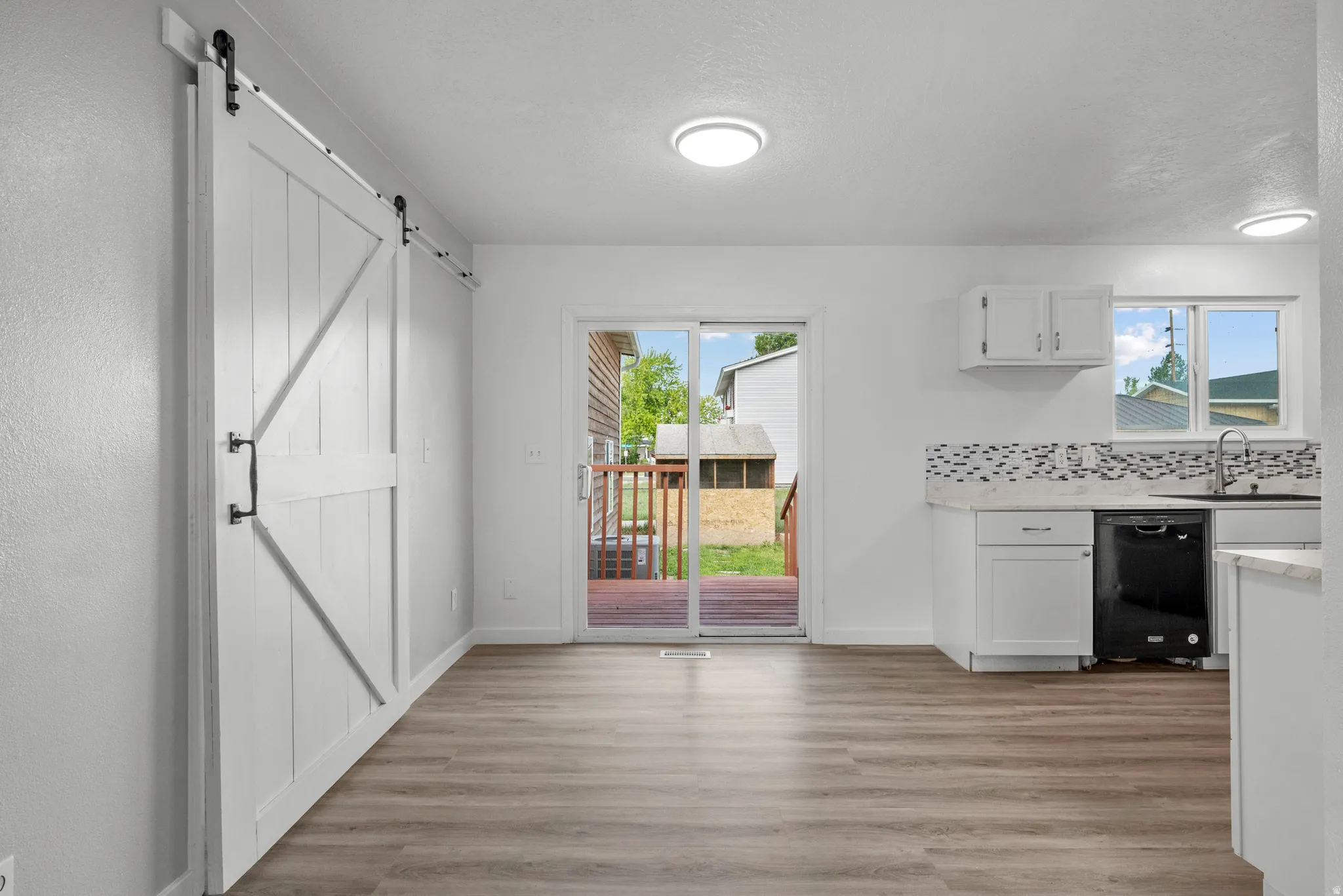 Open-concept living area featuring wood-finish flooring, a contemporary white barn door, and sliding glass doors opening to an outdoor deck