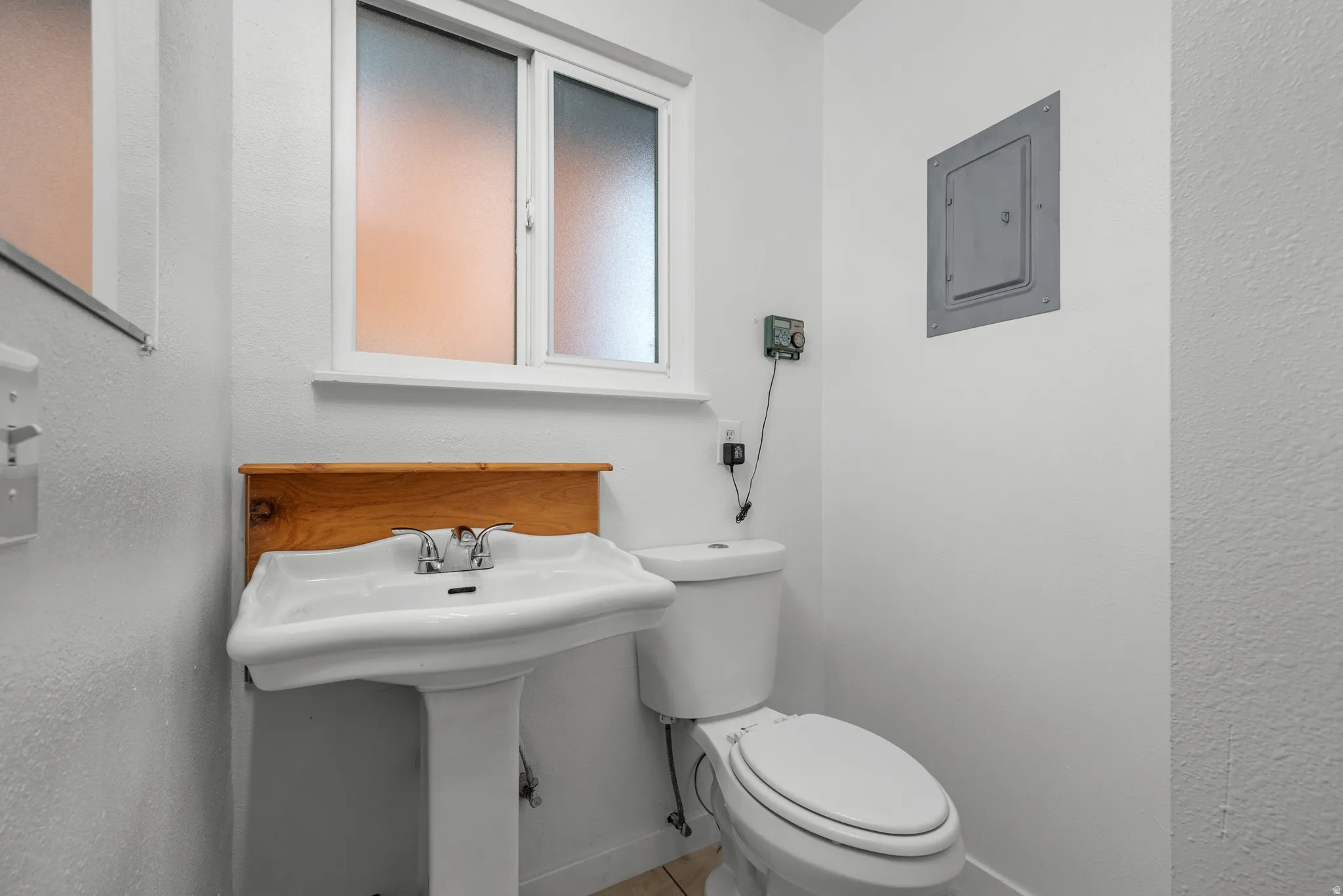 Pedestal sink with chrome faucet set against a wooden backsplash