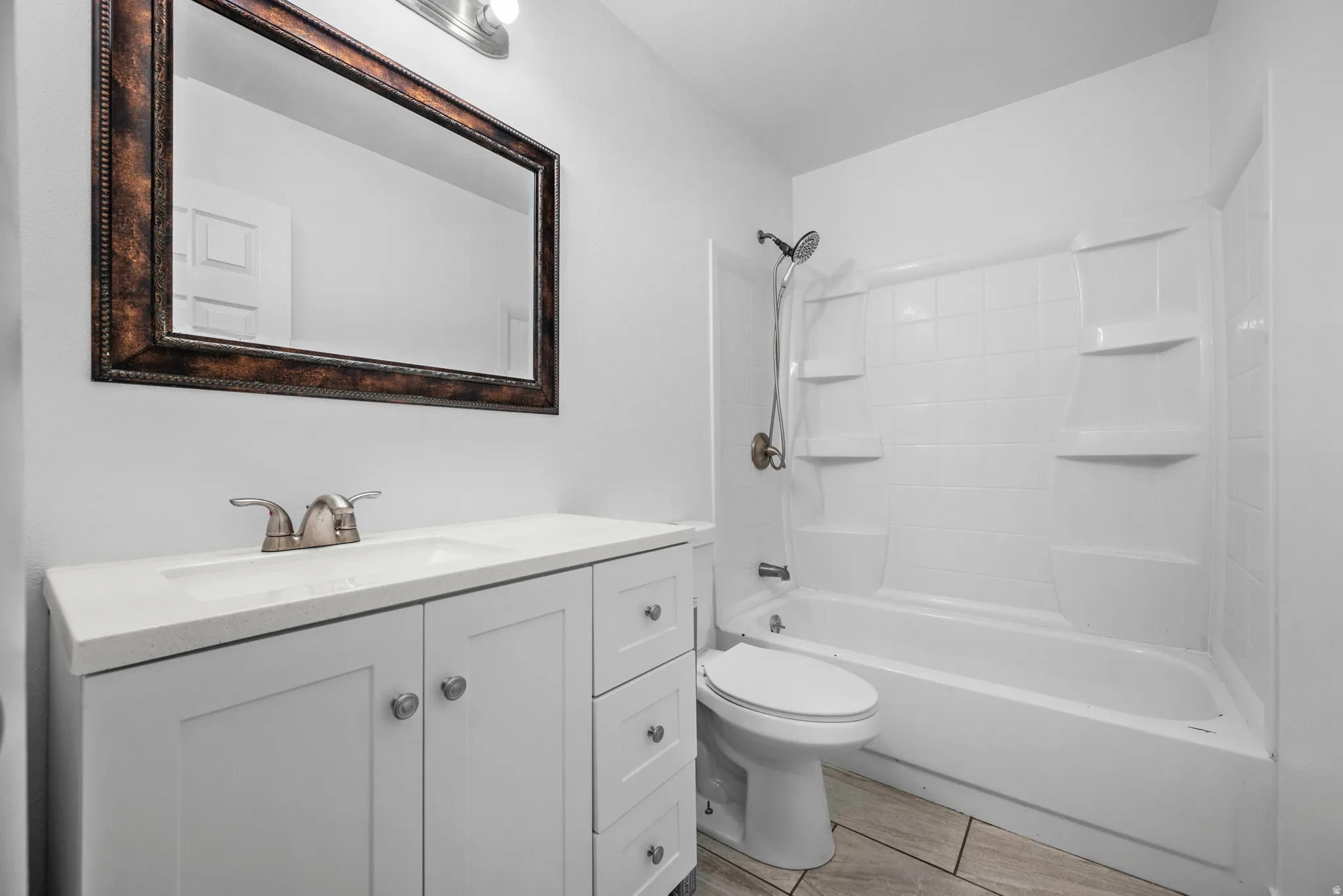 Bathroom featuring a single vanity with a white countertop and undermount sink, a framed mirror, and a white tub/shower combination with integrated shelving
