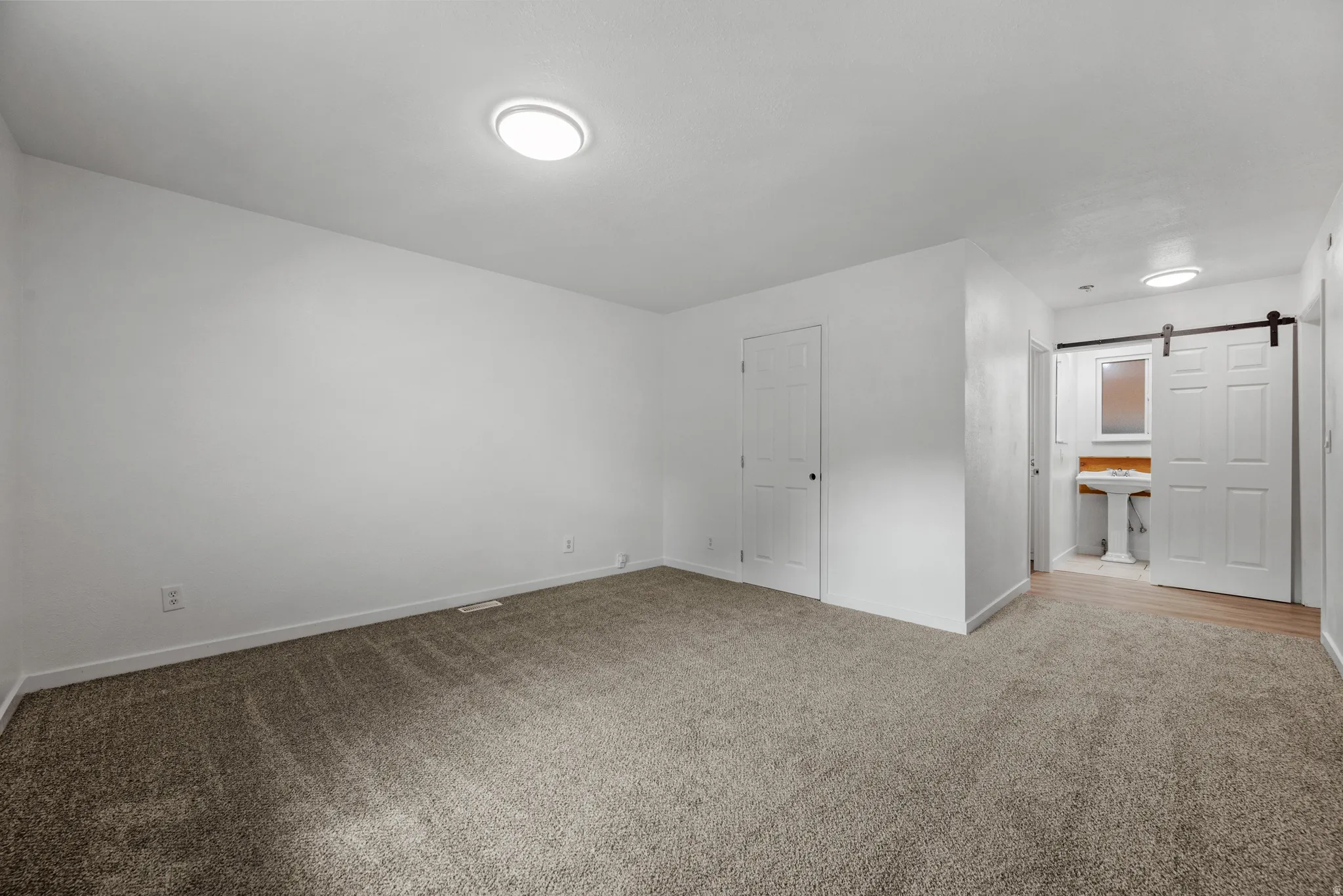 Carpeted room with white walls, ceiling-mounted lighting, and a white interior door