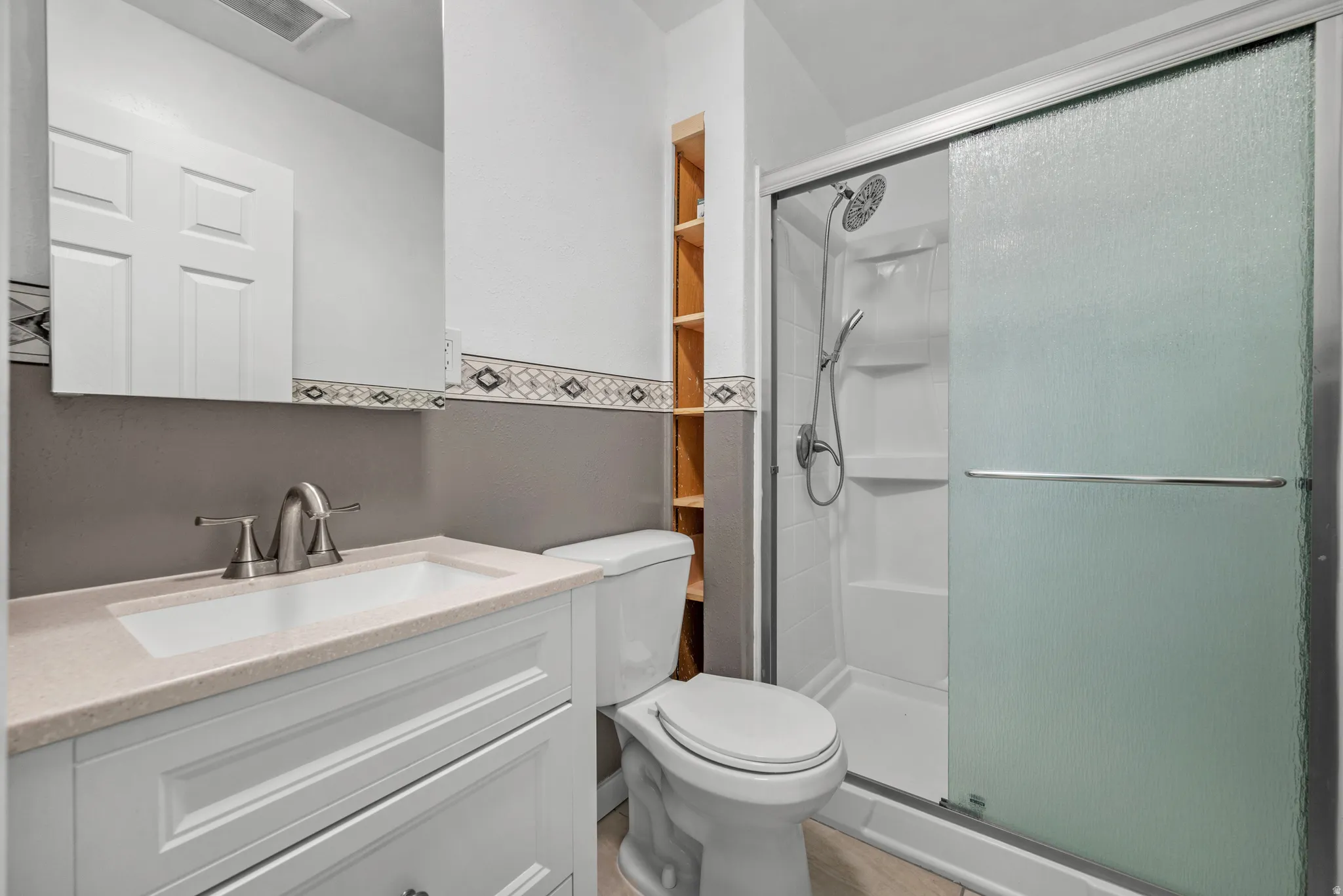 Bathroom featuring a white vanity with a light-toned countertop, a shower with sliding frosted glass doors, and built-in shelving