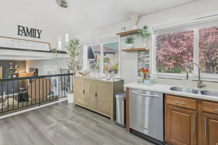 Kitchen with open shelves, stainless steel dishwasher, vaulted ceiling, light wood finished floors, and healthy amount of natural light